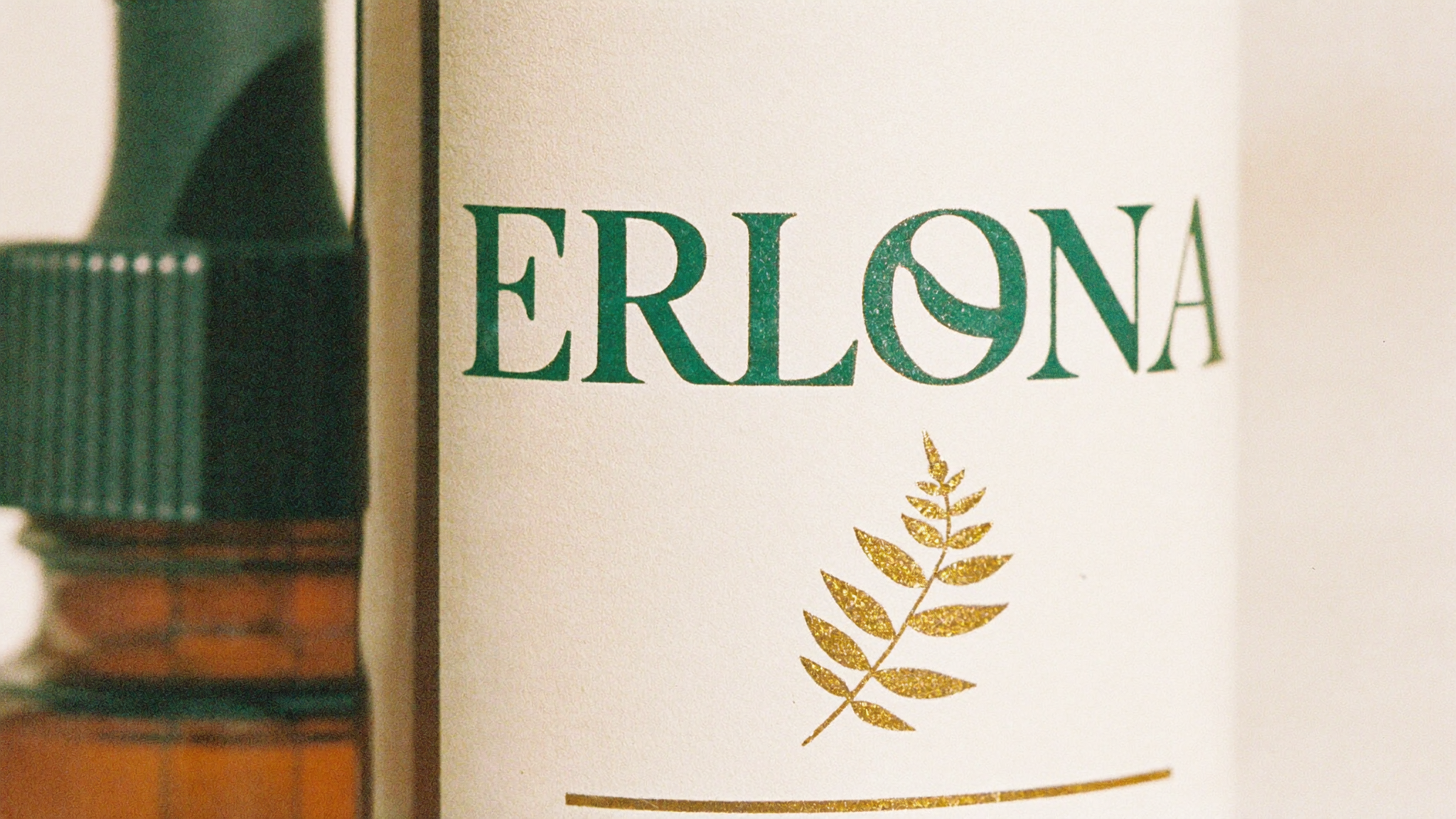 Gros plan de l'étiquette Erlona : nom en capitales serif vert profond et feuille dorée sur papier crème